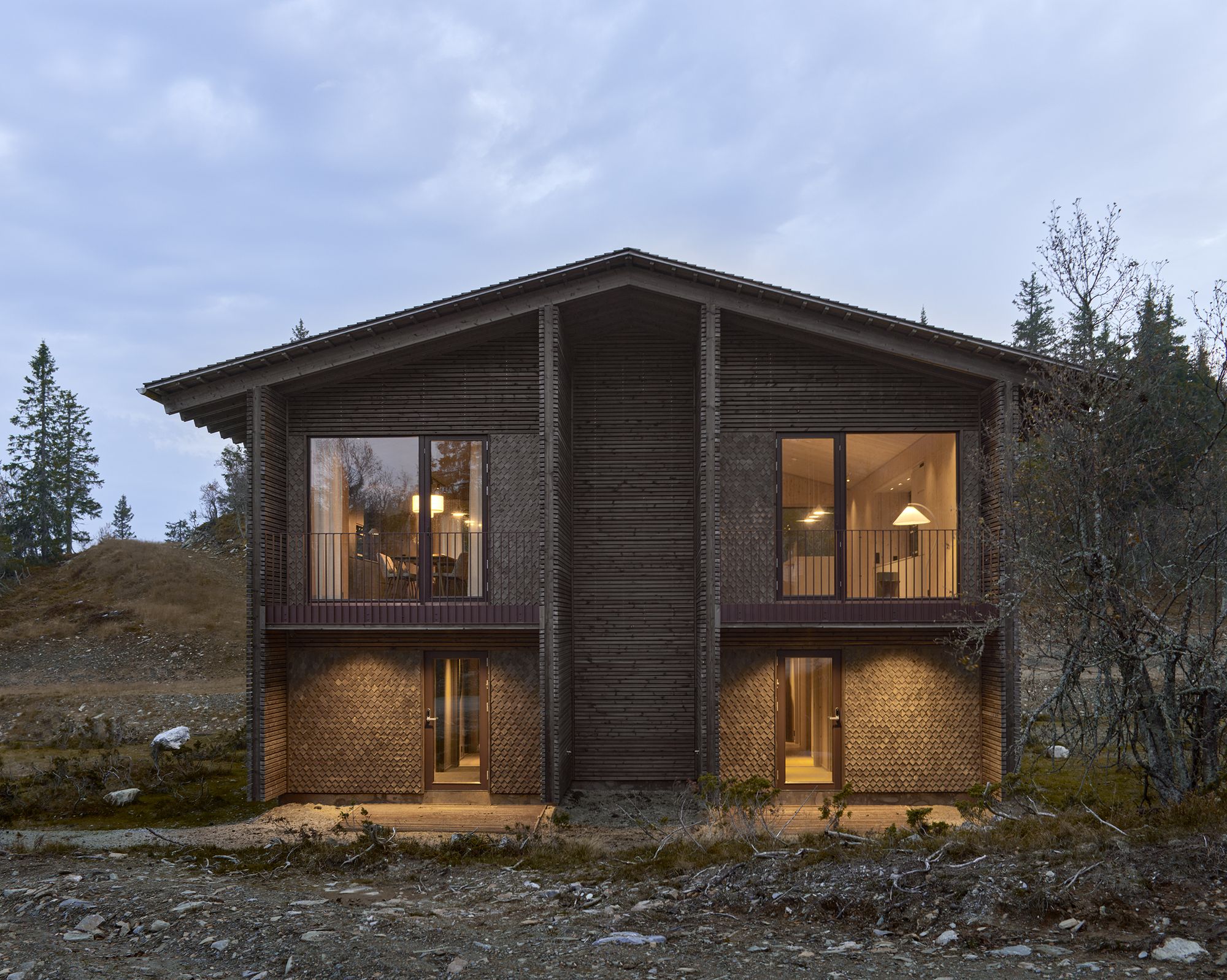Moderne hytte med opplyste vinduer i skumringen